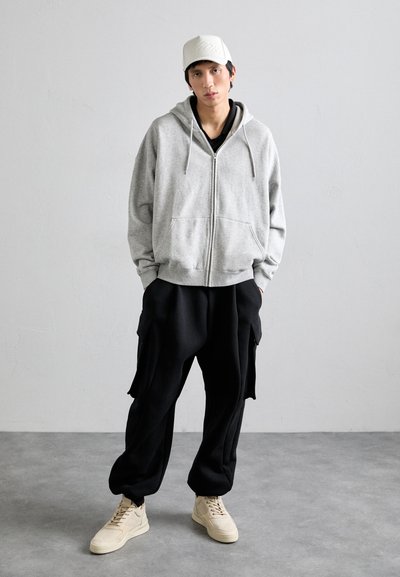 Gray zip-up hoodie with drawstrings, black baggy cargo pants, and beige sneakers. Simple design, casual fit, soft fabric texture.