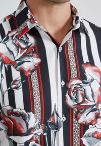 Chemise à manches courtes avec un motif rayé noir et blanc, des illustrations de roses rouges et blanches, et des accents décoratifs à motifs sur le col.