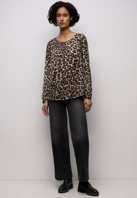 Bluzka z długim rękawem w panterkę, wykonana z lekkiego materiału, zestawiona z wysokim stanem, luźnymi czarnymi dżinsami i botkami za kostkę.