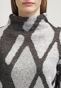 Sweter z dzianiny z wysokim kołnierzem, z geometrycznym czarno-białym wzorem, miękką teksturą i luźnym krojem.