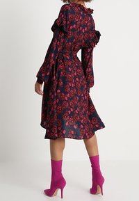 Vestido azul marino con estampado floral, mangas con volantes, cintura ajustada y falda hasta la rodilla. Combinado con botas de tobillo rosa brillante.