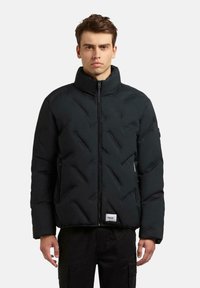 Zwarte pufferjack met hoge kraag, voorzien van diamantstiksel, ritssluiting en zijzakken. Textuurafwerking en merketiket aan de onderrand.