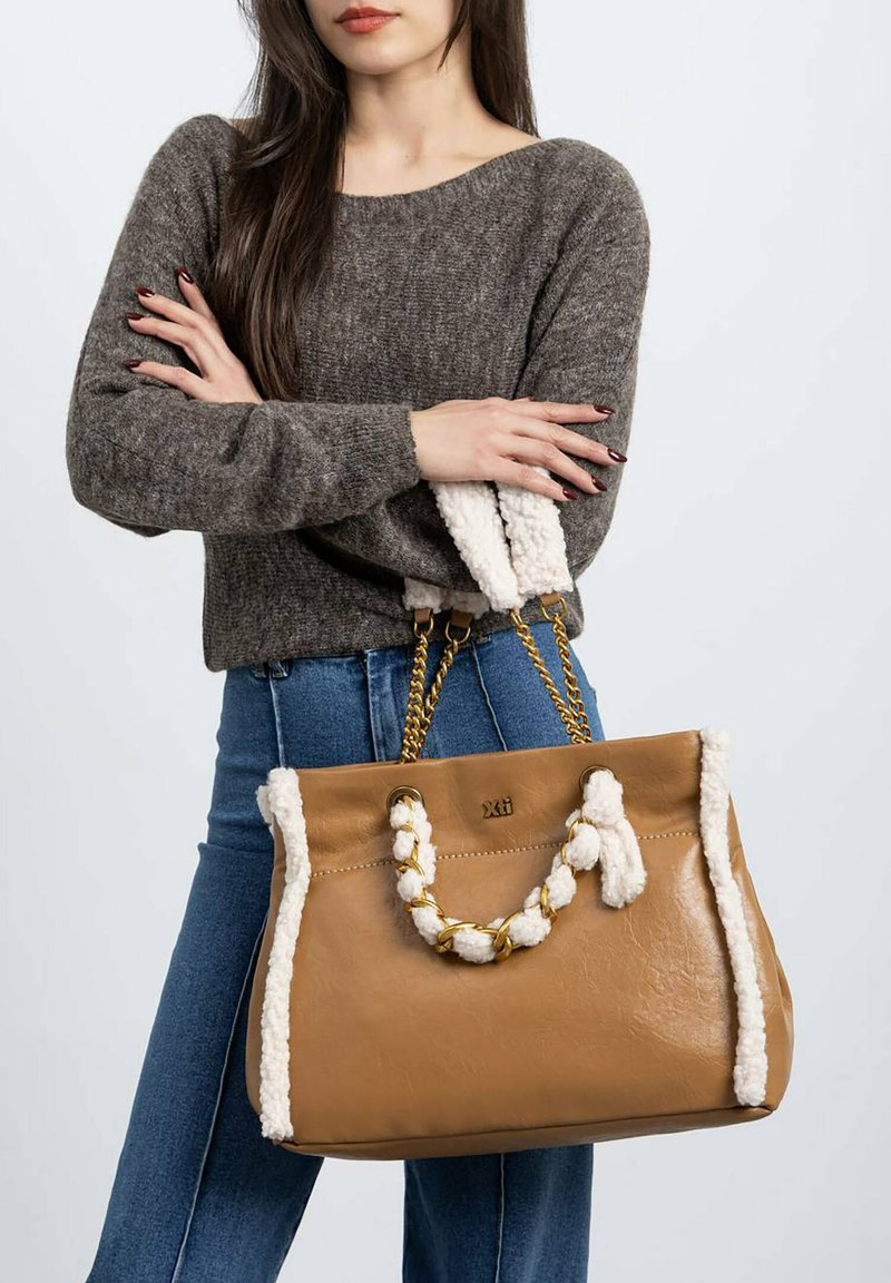 Bolso de cuero marrón claro con ribete texturizado blanco y asa trenzada, presenta herrajes en tono dorado y un diseño espacioso.