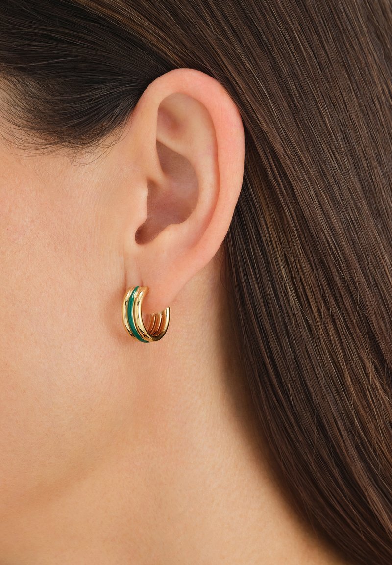 Pendientes de aro dorados y verdes con un diseño en capas y superficies lisas y reflectantes, llevados en una oreja perforada.