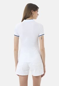Polo shirt bianco con un design aderente, maniche corte e dettagli in blu navy sul colletto e i bordi delle maniche. Tessuto in cotone liscio.