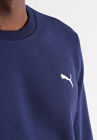 Námořnická modrá mikina vyrobená z jemné látky, s kulatým výstřihem a malým bílým logem Puma na levé části hrudi.
