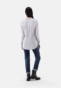 Helles graues Langarmshirt mit einem Rückenfalten, kombiniert mit dunkelblauen Jeans mit umgeschlagenem Saum und schwarzen Ankle-Boots mit einem Schnallendetail.