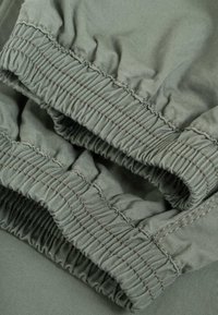Close-up of green fabric with elasticated, gathered cuffs and visible stitching detail.
