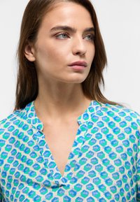 Lightweight, patterned blouse in blue and green hexagonal shapes; features a subtle collar and a loose fit for comfort.