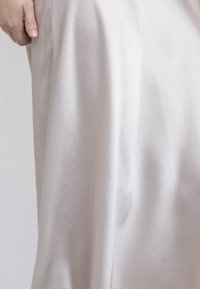 Jupe en satin d'un ivoire clair, présentant une texture lisse et un design fluide. Comprend un drapé subtil et une taille ajustée.