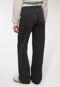 Jeans neri a gamba larga con vita alta, dotati di due tasche posteriori e orlo pulito. Il tessuto sembra robusto e ha una superficie liscia.