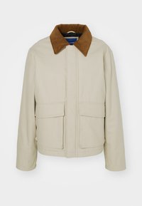 Veste en coton beige avec un col en velours côtelé marron, dotée d'une fermeture éclair à l'avant et de deux grandes poches plaquées. Texture lisse, forme carrée.