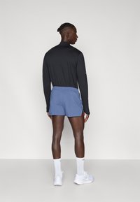 Μαύρη μπλούζα με μακριά μανίκια και μπλε σορτς. Τα σορτς είναι ελαφριά με ελαστική μέση. Φοριούνται λευκά αθλητικά παπούτσια και κάλτσες.