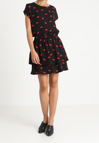 Black dress featuring red lip print, short sleeves, loose-fitting top, elastic waist, and layered ruffle skirt. Worn with black mules.