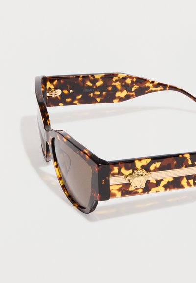 Lunettes de soleil rectangulaires en écaille de tortue avec des verres bruns et un détail logo Médusa doré sur les branches épaisses.