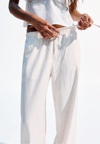 Ljust beige linnebyxor med avslappnad passform, elastisk midja med dragsko och sidofickor, visade mot en vit bakgrund.