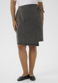 Naine kannab põlvekohale ulatuvat tumashalli ümbrikku, mis on vöökoha pealt seotud, mustade baleriinatudede ja valge särgiga.