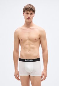 Biele bavlnené boxerky s čiernym elastickým pásom Levi's, s priliehavým strihom a hladkou textúrou, nosené osobou stojacou vzpriamene.