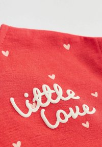 Piros szövet fehér hímzett szöveggel, amelyen az szerepel: "kis szerelem", apró világos rózsaszín szívek veszik körül. Puha textúra és laza kialakítás.
