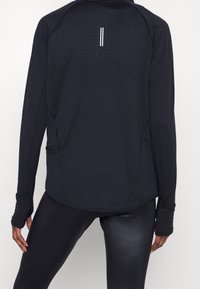 Donned langemouw performance t-shirt in donker marineblauw, met een ronde zoom, duimopeningen in de mouwen en reflecterende accenten op de rug.