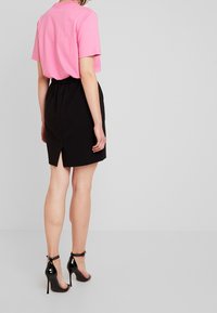 Maglietta rosa a maniche corte abbinata a una gonna nera con uno spacco sul retro. Design aderente, trama liscia e sandali neri con tacchi alti lucidi.