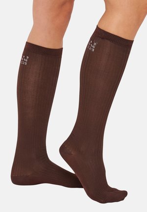 Pruunid põlvikud, mis ulatuvad kuni põlveni ja millel on sooniline tekstuur. Neil on tugevdatud varbad ja äär, külgadel valged numbrid.