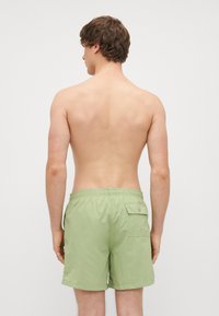 Heledad rohelised ujumispüksid sünteetilisest materjalist, millel on elastne vöökoht ja tagumine tasku klapiga.