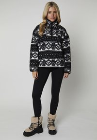 Pullover in pile con motivo in bianco e nero, con colletto a mezza zip, abbinato a leggings neri e stivali foderati in pelliccia beige.