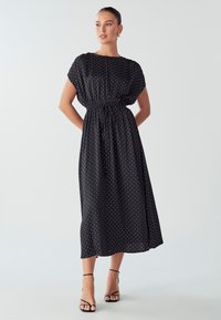 Schwarzes Midi-Kleid mit Punkten, kurzen Ärmeln, elastischem Taillenbund und leichtem Stoff. Es zeichnet sich durch eine lockere Passform und einen fließenden Schnitt aus.