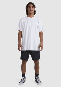 T-shirt en coton blanc au coupe décontractée, assorti avec un short noir et des baskets montantes noires. Design simple, sans graphiques ni logos visibles.