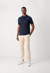 Marineblå polo skjorte, korte ærmer, krave; kombinert med lys beige chinos og hvite joggesko; glatt stoff, tilpasset passform.