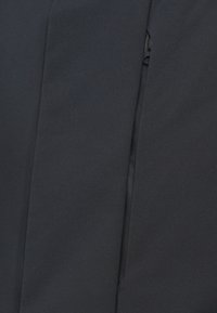 Černý textilní oděv s hladkou texturou. Obsahuje viditelný zip podél švu, který posiluje štíhlý, těsně přiléhající design.