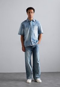 Lys blå denimskjorte med korte ermer og brystlomme, kombinert med lys blå vide bukser. Hvite sneakers fullfører antrekket.