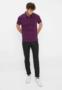 Polo shirt in dieppaars katoen met contrasterende witte kraag en mouwranden, gecombineerd met zwarte broek en witte sneakers.