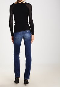 Zwarte geribbelde langemouwen top met een open rug, gecombineerd met donkerblauwe slim-fit jeans met subtiele stiksels en een logo op de achterzak.
