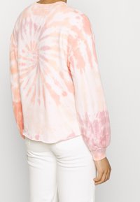 Maglietta a maniche lunghe in tie-dye nei toni pastello di rosa e pesca, caratterizzata da un motivo a spirale circolare e polsini a coste. Tessuto morbido; vestibilità rilassata.