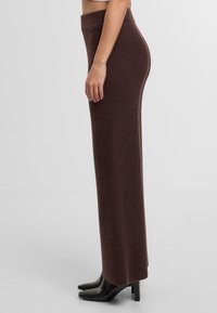 Hnědá pletená maxi sukně s přiléhavým pasem, dlouhým siluetou a texturovanou tkaninou, spárovaná s černými špičatými podpatky.