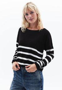 Gestreifter schwarz-weißer Pullover mit lockerer Passform, gerippten Bündchen und Rundhalsausschnitt, kombiniert mit hoch taillierten blauen Jeans.