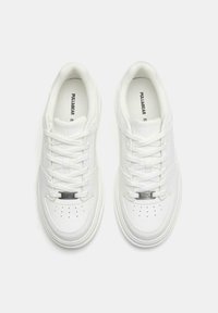 Weiße Sneaker mit einem glatten Lederoberteil, runder Spitze, perforierten Details und flachen Schnürsenkeln. Silberfarbene Metallakzente an der Zunge.