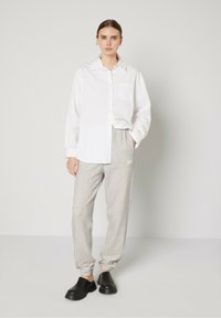 Chemise blanche à boutons avec une poche, associée à un pantalon de jogging gris portant un logo et des sabots noirs. Tenue simple et décontractée avec une coupe relax.