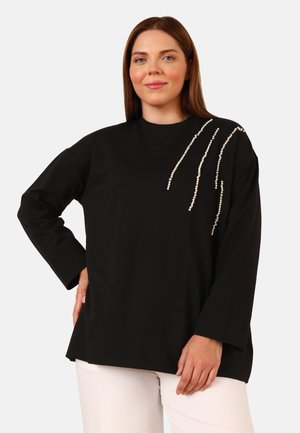 Haut noir à manches longues en tissu doux, orné de détails en perles blanches asymétriques sur l'épaule et avec une coupe décontractée.