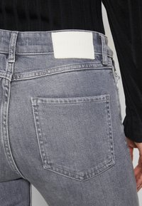 Jeans de denim gris con un bolsillo trasero y una etiqueta de tela blanca con "Marc O’Polo DENIM" cosida en la cintura.