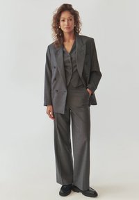 Grijze op maat gemaakte driedelige pak met een dubbelzijdige blazer, een aangesloten vest met knopen en wijde broeken. Glad textuur, subtiel ruitpatroon.