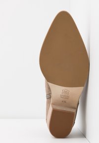 Suola di scarpa in suede beige con forma arrotondata e bordo in gomma testurizzata. Presenta dettagli in cuoio goffrato e accenti di colore crema.