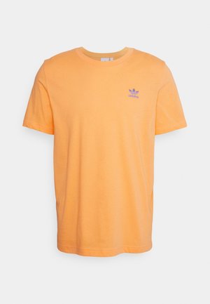 Jasno pomarańczowa koszulka Adidas z krótkim rękawem, z małym fioletowym logo Adidas na lewej piersi i okrągłym dekoltem.