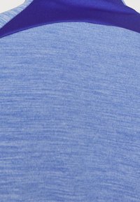 Kortærmet sportsbluse i lyseblåt stof med en glat, struktureret overflade; har en mørkeblå detalje ved kraven.