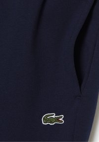 Marineblauer Pullover mit weicher Textur und geripptem Abschluss, mit einem grünen und weißen, gestickten Krokodil-Logo auf der linken Seite.