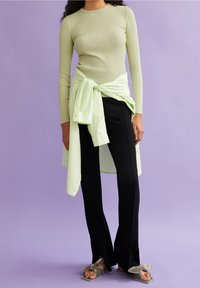 Prążkowana bluzka z długim rękawem w jasnym zielonym kolorze, zestawiona z czarnymi spodniami typu dzwony. Przewiewna, jasna zielona koszula w oversize'u związaną w talii. Miękkie szare sandały z kokardkami.