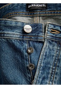 Jeans din denim cu o spălare albastră deschisă. Au un sistem de închidere cu nasturi, accesorii argintii, cusături galbene și un eticheta neagră cu "JACK & JONES."