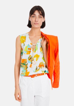 Ärmellose Bluse mit floralem Muster in mehreren Farben, weißer Grundfarbe und verstellbarem Kordelzug. Kombiniert mit einem leuchtend orangefarbenen Blazer und einem Gürtel.